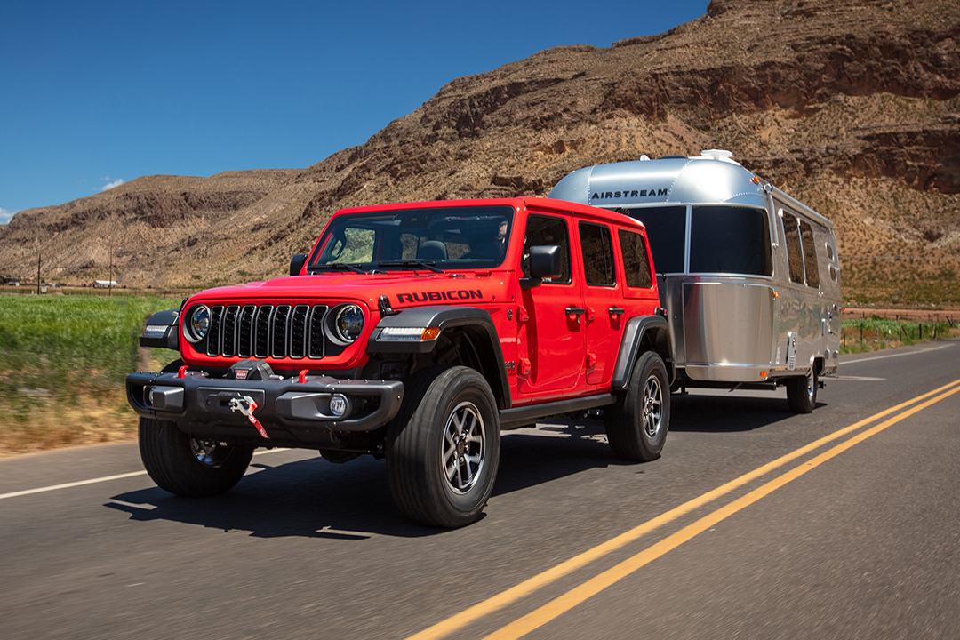 Front side view of Jeep Wrangler 2024 on road with trailer in tow